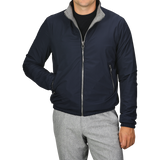 A person dressed in the Manto Navy Grey Cashmere Nylon Reversible Blouson with grey trim and light grey pants. The blouson is zipped up, and the person has their left hand in their pocket, with their face out of view.