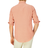 A person standing with their back to the camera, wearing a pink Massimo Alba Peach Orange Striped Cotton Linen Genova Shirt with rolled-up sleeves.