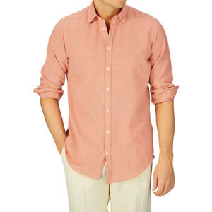 Man wearing a Massimo Alba Peach Orange Striped Cotton Linen Genova Shirt and cream pants against a grey background.