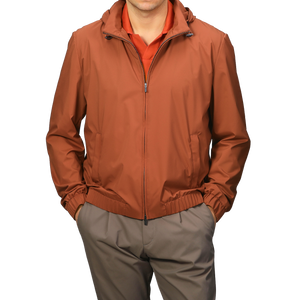 A man wearing a Terracotta Brown Nylon Hooded Blouson Jacket by Maurizio Baldassari over a red shirt, paired with khaki pants.