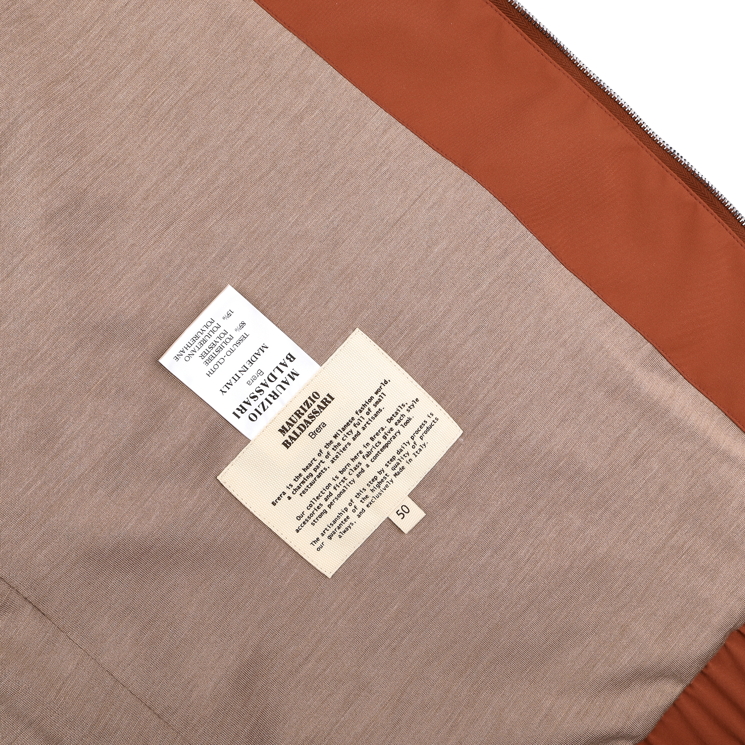 Close-up of a Terracotta Brown Nylon Hooded Blouson Jacket by Maurizio Baldassari, featuring two labels on sleek technical nylon that include care instructions, material details, and size information.