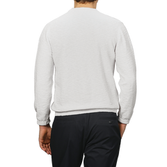 A person in a Cream Summer Mouline Crew Neck Sweater by Maurizio Baldassari and dark pants, viewed from the back, stands against a gray background.