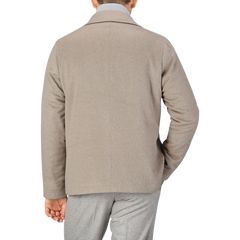 A person is shown from the back wearing a beige cashmere half padded chore coat by Maurizio Baldassari and grey pants against a plain background.