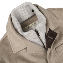 The Beige Cashmere Half Padded Chore Coat by Maurizio Baldassari features a white knitted inner lining and black zipper detail. It boasts a fabric label that reads "made in Italy," an outer pocket with a leather accent, and includes a detachable wool-cashmere waistcoat for versatile wear.