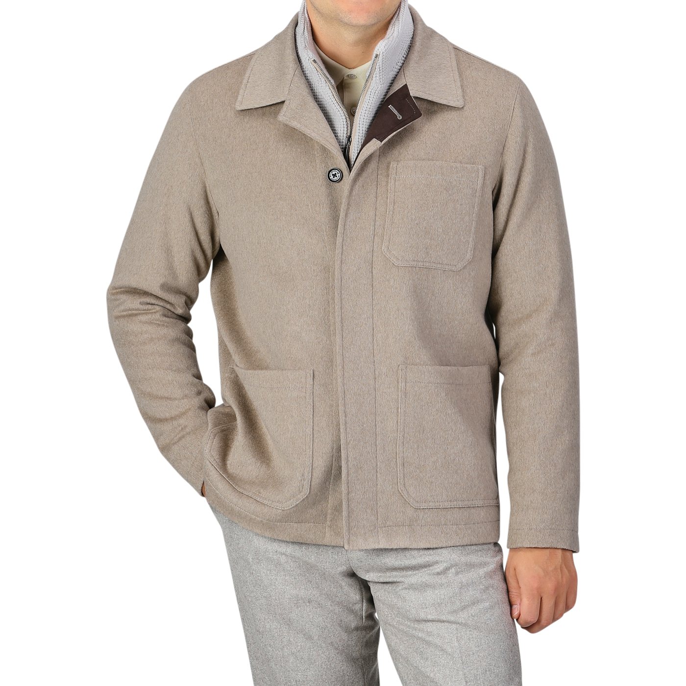 A person is wearing a Beige Cashmere Half Padded Chore Coat by Maurizio Baldassari with three pockets over a light grey shirt, complemented by grey trousers. The ensemble features a detachable wool-cashmere waistcoat peeking out, adding an extra layer of sophistication. Their head is not visible in the image.