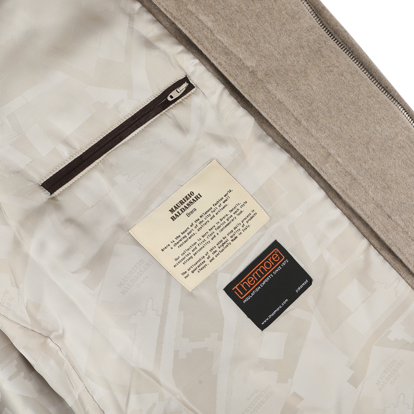 Close-up of a garment's interior revealing two labels sewn onto the fabric—one with care instructions and the other displaying the brand "Maurizio Baldassari." A zipper pocket is also partially visible, reminiscent of details you'd find in a high-end Beige Cashmere Half Padded Chore Coat.