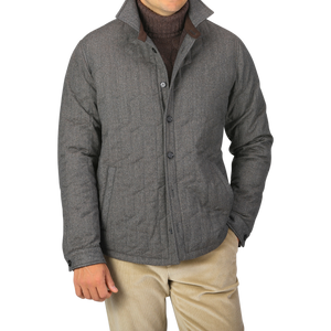 A person wearing a Maurizio Baldassari Taupe Beige Herringbone Quilted Virgin Wool Overshirt over a dark sweater and light-colored pants, with their hands partially in their pockets.