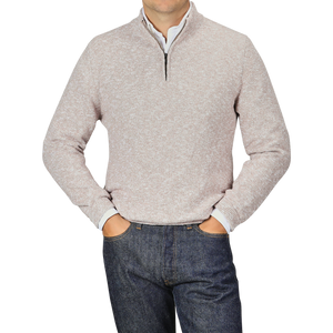 A person is wearing a Beige Winter Wool Mouline 1/4 Zip Sweater by Maurizio Baldassari and dark blue jeans, with their hands resting in their pockets. The background is a plain light gray color.