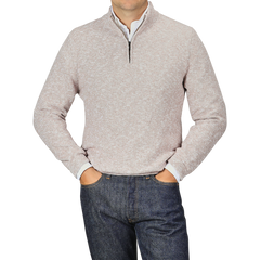 A person is wearing a Beige Winter Wool Mouline 1/4 Zip Sweater by Maurizio Baldassari and dark blue jeans, with their hands resting in their pockets. The background is a plain light gray color.