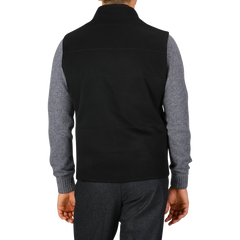 A rear view of a person wearing a Maurizio Baldassari Black Water Repellent Cashmere Gilet over a gray long-sleeve shirt and dark pants, standing against a white background.