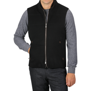 A person is wearing a Black Water Repellent Cashmere Gilet from Maurizio Baldassari over a gray long-sleeve shirt and dark pants. The gilet, featuring side pockets, adds a touch of sophistication as the person poses with one hand in a pocket.