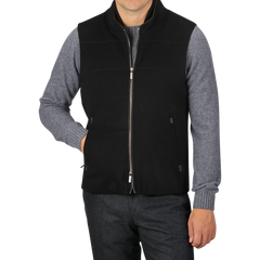 A person is wearing a Black Water Repellent Cashmere Gilet from Maurizio Baldassari over a gray long-sleeve shirt and dark pants. The gilet, featuring side pockets, adds a touch of sophistication as the person poses with one hand in a pocket.