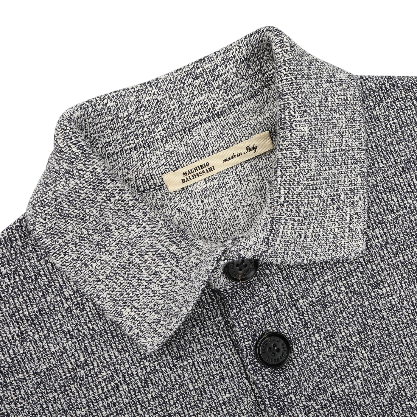 A close-up of the Blue Melange Summer Mouline Blouson by Maurizio Baldassari reveals a hint of flair, featuring two black buttons and a beige "Made in Italy" label. The cotton-viscose blend fabric showcases a speckled pattern for added depth.