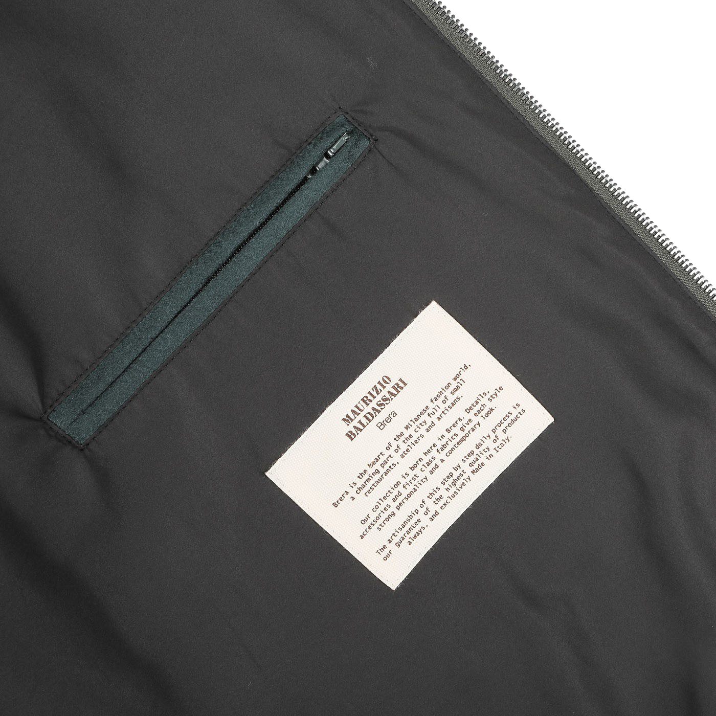 Close-up of an open zipper on a Maurizio Baldassari Bottle Green Cashmere Zip Blouson, showcasing a dark pocket on the left and a white label with text on the right.