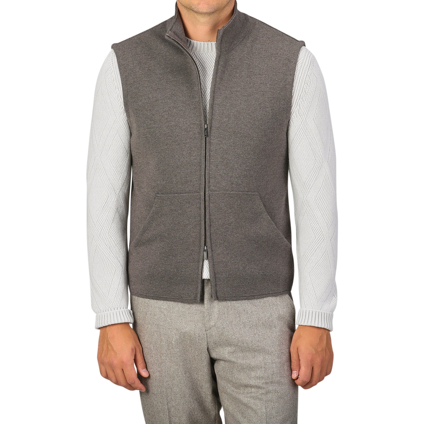 A person is wearing a Brown Melange Milano Stitch Wool Zip Gilet by Maurizio Baldassari over a white sweater with patterned sleeves made from pure virgin wool and gray pants, standing against a plain background.