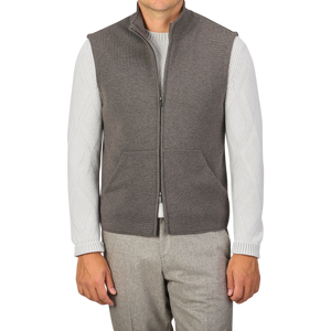 A person is wearing a Brown Melange Milano Stitch Wool Zip Gilet by Maurizio Baldassari over a white sweater with patterned sleeves made from pure virgin wool and gray pants, standing against a plain background.