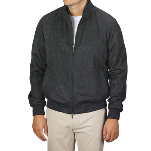 A person is standing against a plain background wearing a Maurizio Baldassari Charcoal Grey Cashmere Zip Blouson, fully zipped with a high collar, paired with beige pants. The person's face is not visible.