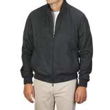 A person is standing against a plain background wearing a Maurizio Baldassari Charcoal Grey Cashmere Zip Blouson, fully zipped with a high collar, paired with beige pants. The person's face is not visible.