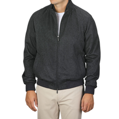 A person is standing against a plain background wearing a Maurizio Baldassari Charcoal Grey Cashmere Zip Blouson, fully zipped with a high collar, paired with beige pants. The person's face is not visible.