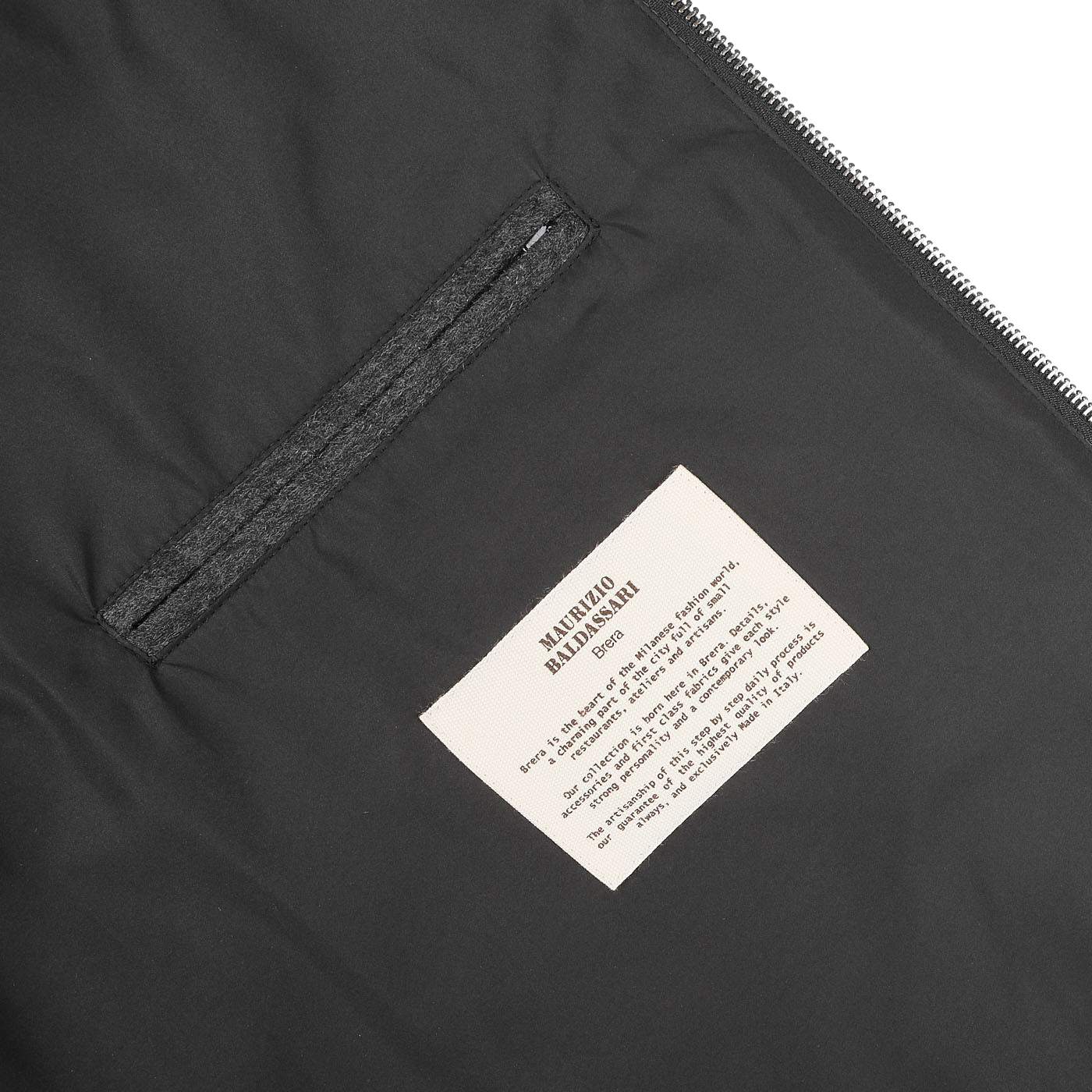 A detailed view of the interior lining of the Charcoal Grey Cashmere Zip Blouson by Maurizio Baldassari, showcasing a fabric label with text and a small zippered pocket.