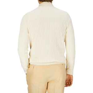 Rear view of a person wearing a Maurizio Baldassari cream cotton silk cable knit 1/4 zip sweater and light beige trousers.