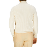 Rear view of a person wearing a Maurizio Baldassari cream cotton silk cable knit 1/4 zip sweater and light beige trousers.