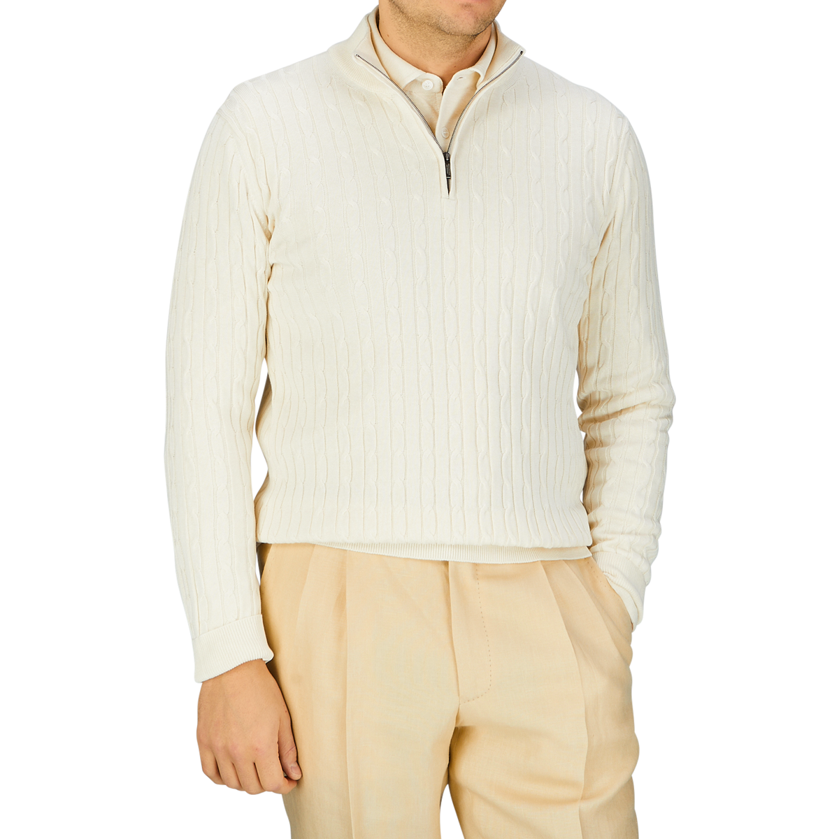 A person wearing a Cream Cotton Silk Cable Knit 1/4 Zip Sweater crafted by Maurizio Baldassari, with a zipper collar and light beige trousers.