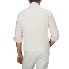 A man is shown from behind wearing a Maurizio Baldassari Cream Milano Stitch Wool Zip Gilet, a light-colored rolled-up sleeve shirt, and cream-colored pants.