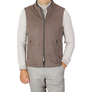 A person dressed in a gray long-sleeve shirt under a sleeveless, zip-up Dark Taupe Water Repellent Cashmere Gilet from Maurizio Baldassari, with their right hand in their pocket. They are also wearing gray trousers. The stylish ensemble features pieces like the water-repellent vest, blending practicality and elegance seamlessly.