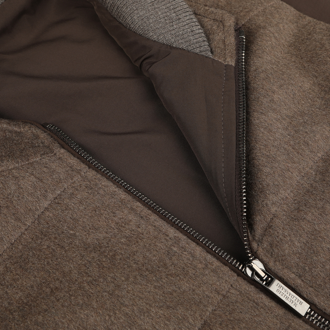 Close-up view of an open brown jacket with a visible metal zipper and dark inner lining, layered over a Maurizio Baldassari Dark Taupe Water Repellent Cashmere Gilet.