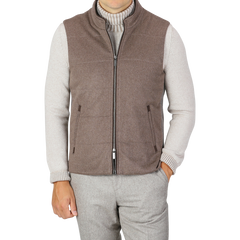 A person dressed in a gray long-sleeve shirt under a sleeveless, zip-up Dark Taupe Water Repellent Cashmere Gilet from Maurizio Baldassari, with their right hand in their pocket. They are also wearing gray trousers. The stylish ensemble features pieces like the water-repellent vest, blending practicality and elegance seamlessly.