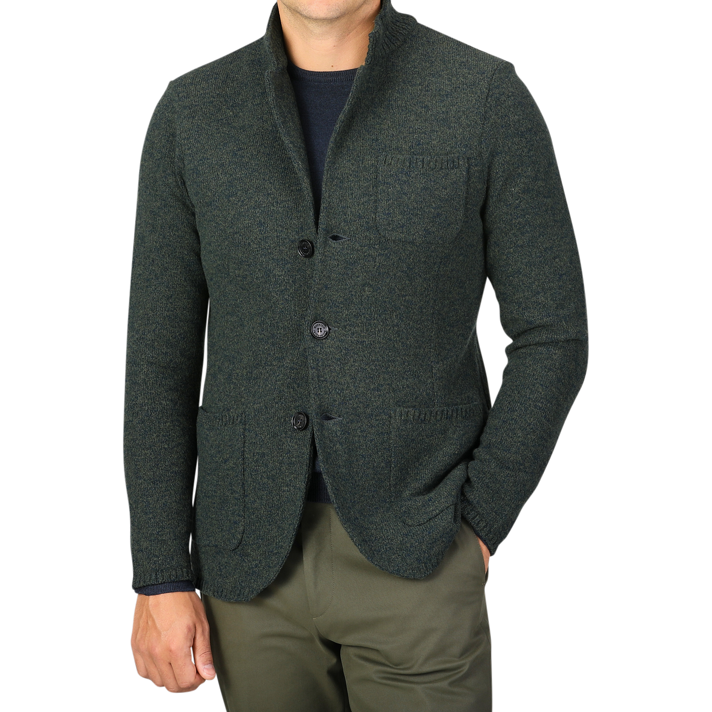 A person wearing Maurizio Baldassari's Green Melange Winter Wool Mouline Swacket, made from a luxurious wool-cotton blend, over a navy shirt and olive green pants stands against a plain background. The swacket, featuring three buttons and three front pockets, exudes stylish sophistication.