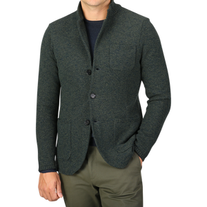 A person wearing Maurizio Baldassari's Green Melange Winter Wool Mouline Swacket, made from a luxurious wool-cotton blend, over a navy shirt and olive green pants stands against a plain background. The swacket, featuring three buttons and three front pockets, exudes stylish sophistication.