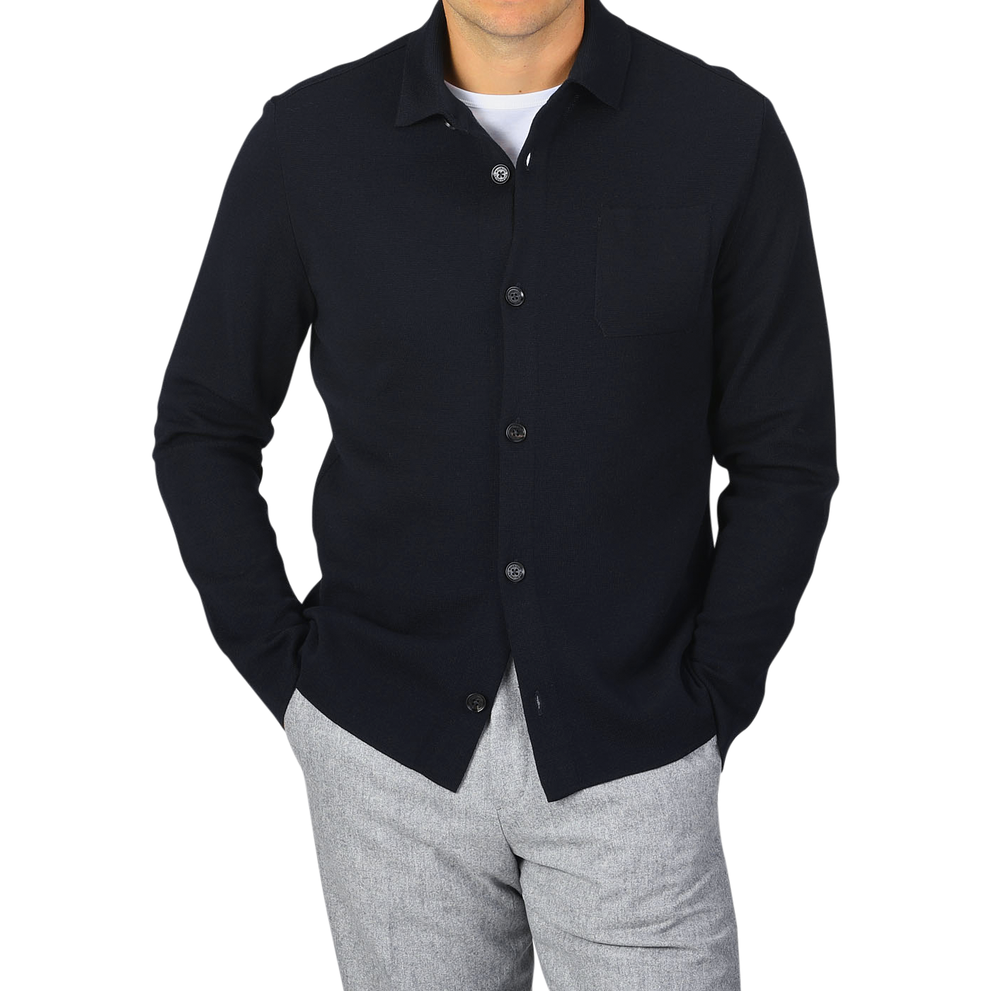 A person wearing a Navy Blue Wool Milano Knitted Overshirt by Maurizio Baldassari with a pocket on the left side and light grey pants, with hands in pockets, standing against a plain grey background.