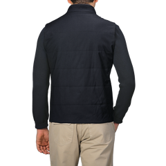 A person is seen from the back, wearing a Maurizio Baldassari Navy Merino Wool Thermore Travel Gilet and beige pants, set against a light gray background.