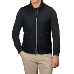 Wearing a Maurizio Baldassari Navy Merino Wool Thermore Travel Gilet over a black long-sleeve shirt and beige pants, an individual stands against a plain background.