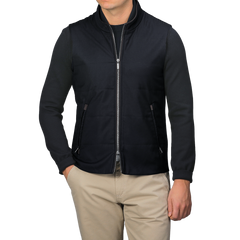 Wearing a Maurizio Baldassari Navy Merino Wool Thermore Travel Gilet over a black long-sleeve shirt and beige pants, an individual stands against a plain background.