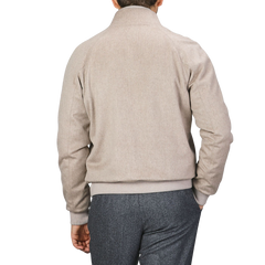 A person wearing a Maurizio Baldassari Oatmeal Beige Cashmere Zip Blouson with ribbed hems and gray trousers is seen from the back, standing against a plain background.