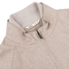 Close-up of an Oatmeal Beige Cashmere Zip Blouson jacket with a high collar by Maurizio Baldassari, featuring a label that reads "Made in Italy" and "Maglificio Gran Sasso." The fabric appears soft and textured, with ribbed hems for added detail.