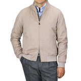 A person dressed in a Maurizio Baldassari Oatmeal Beige Cashmere Zip Blouson with their left hand in the pocket, wearing a blue button-up shirt and gray trousers against a plain background.