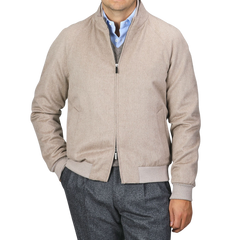 A person dressed in a Maurizio Baldassari Oatmeal Beige Cashmere Zip Blouson with their left hand in the pocket, wearing a blue button-up shirt and gray trousers against a plain background.