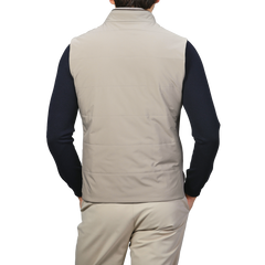 A person wearing a Maurizio Baldassari Pale Beige Nylon Thermore Travel Gilet, paired with beige pants and a navy long-sleeve shirt, seen from the back.