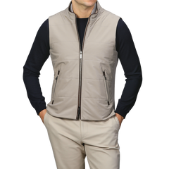 A person stands against a plain background, wearing the Maurizio Baldassari Pale Beige Nylon Thermore Travel Gilet over a black long-sleeve shirt and beige pants.