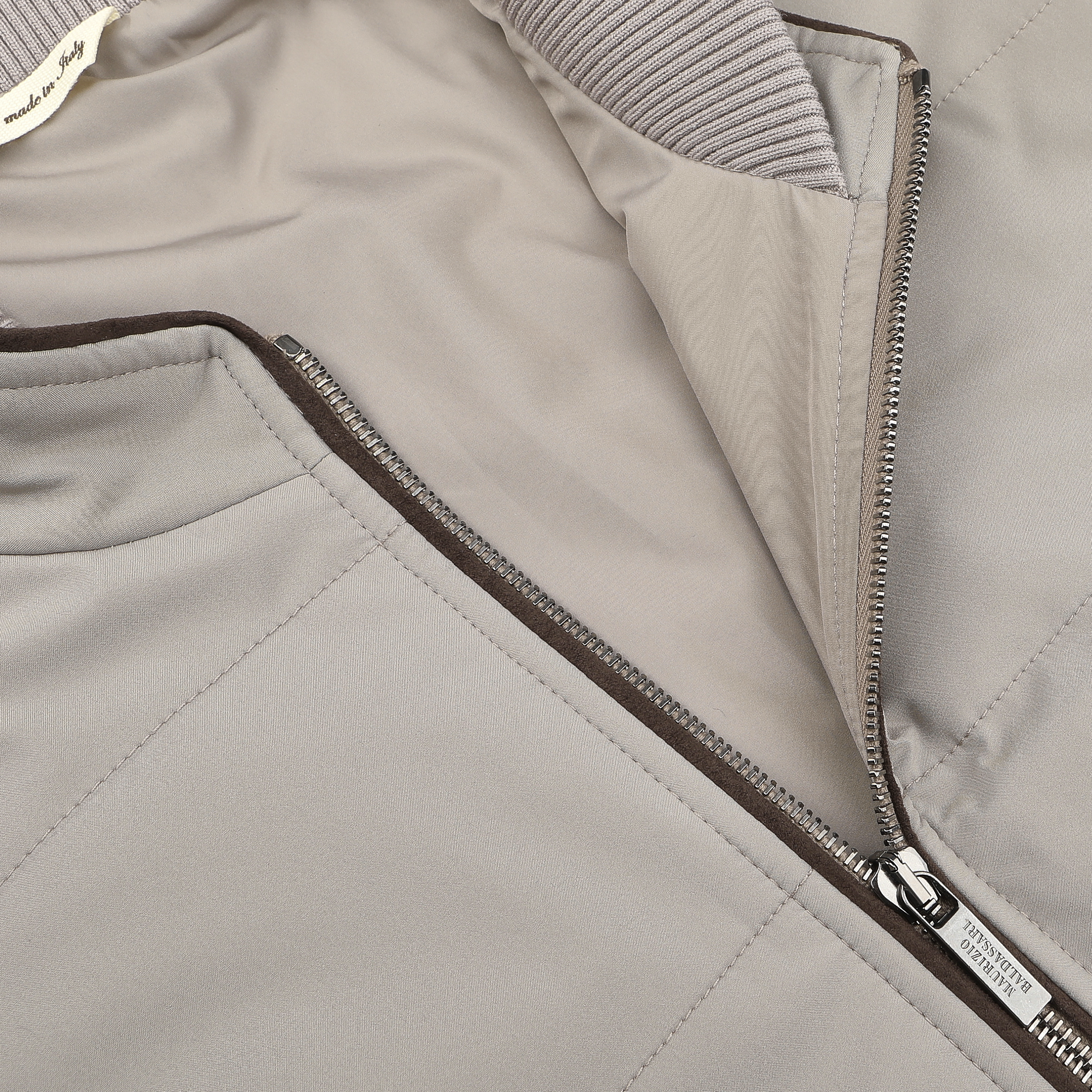 Close-up of a pale beige nylon gilet by Maurizio Baldassari, featuring a visible zipper and ribbed collar detail.