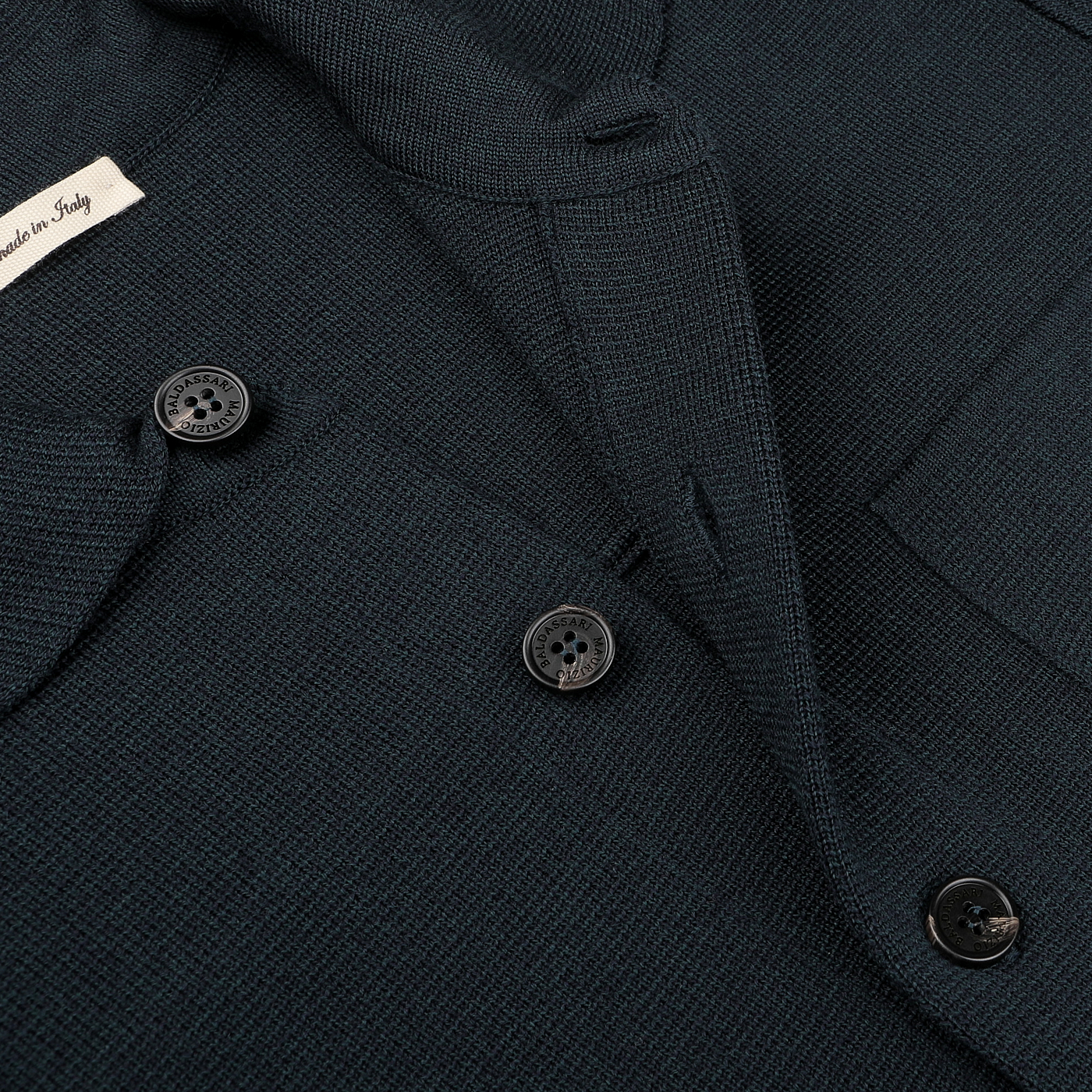 Close-up of a Petrol Green Milano Knitted Wool Overshirt by Maurizio Baldassari, showcasing its dark textured fabric crafted from virgin wool, with three black buttons and a partially visible label reading "Made in Italy.