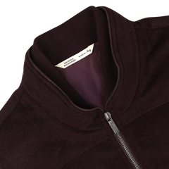 A close-up of a plum water-repellent cashmere gilet from Maurizio Baldassari, featuring a silver zipper and a label inside the collar that reads "Made in Italy." The fabric boasts 100% cashmere, offering luxurious comfort.