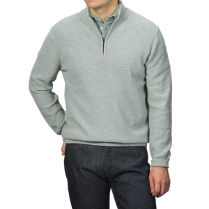 A person models the Sage Green Summer Mouline 1/4 Zip Sweater by Maurizio Baldassari over a green collared shirt and dark jeans, standing against a gray background.