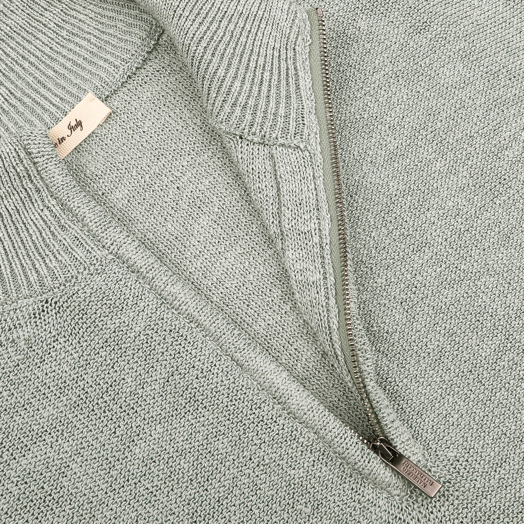 Close-up of a Sage Green Summer Mouline 1/4 Zip Sweater by Maurizio Baldassari, showcasing its half-zip design with a metal zipper and visible tag.