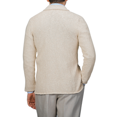 A person in a Sand Beige Summer Mouline Knitted Jacket by Maurizio Baldassari and gray pants is seen from the back against a white background, exuding relaxed luxury.