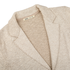 The Sand Beige Summer Mouline Knitted Jacket by Maurizio Baldassari is elegantly displayed, showcasing a cream hue with a notched lapel collar. Crafted from a cotton-viscose blend, it features a textured finish and visible interior label, embodying relaxed luxury.